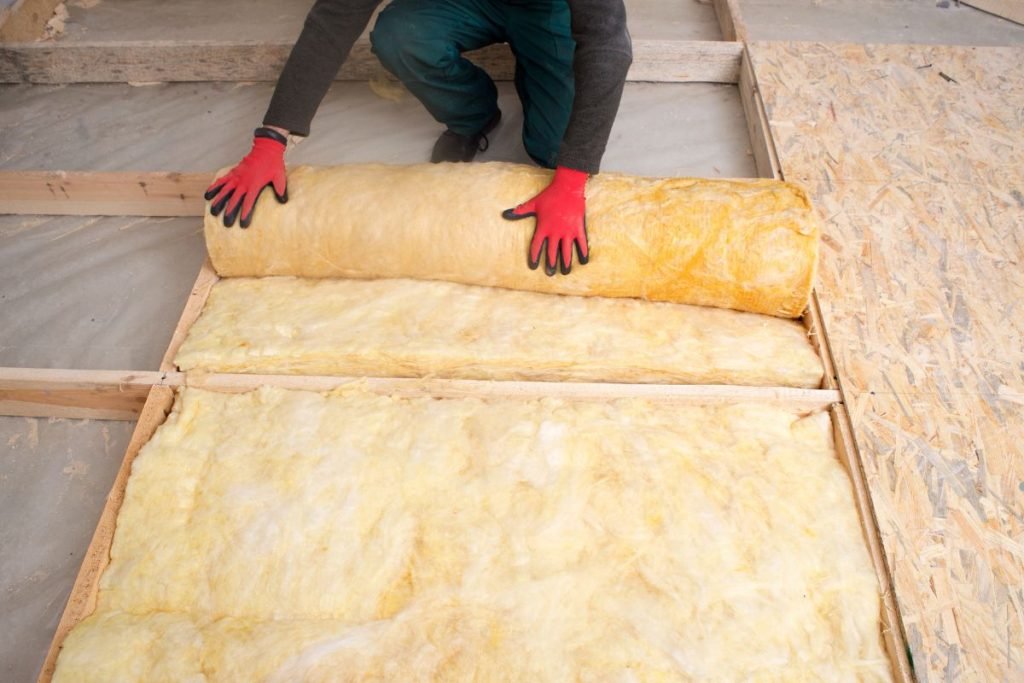 A man laying insulation material on a floor as part of an insulation service project.