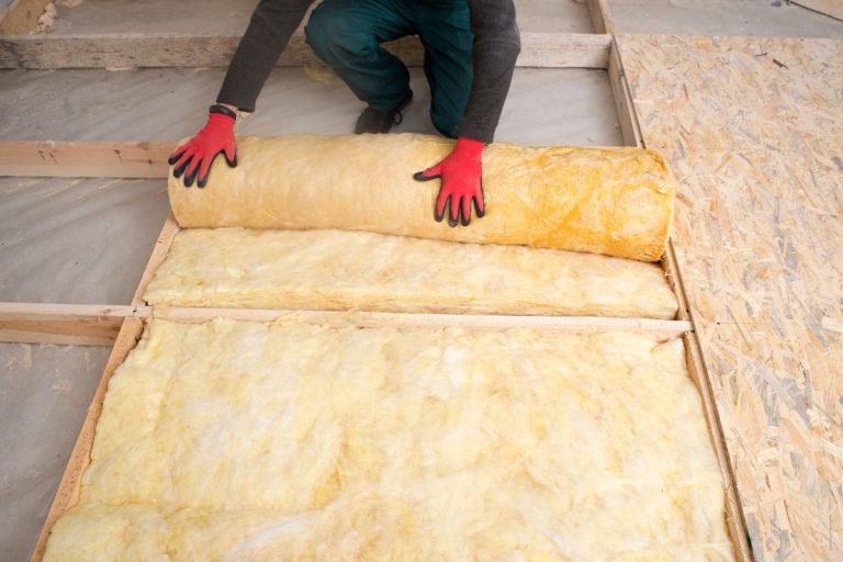A man laying insulation material on a floor as part of an insulation service project.